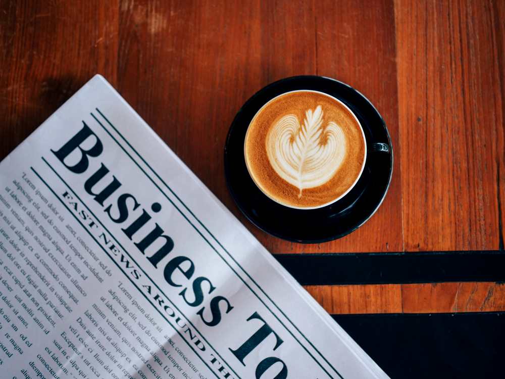 Image of top view of coffee latte art and newspaper in a coffee shop cafe, featuring 411 Corporate Law and highlighting Businesses Going Public (IPO), ensuring it aligns with the page's context on initial public offerings and corporate transitions.